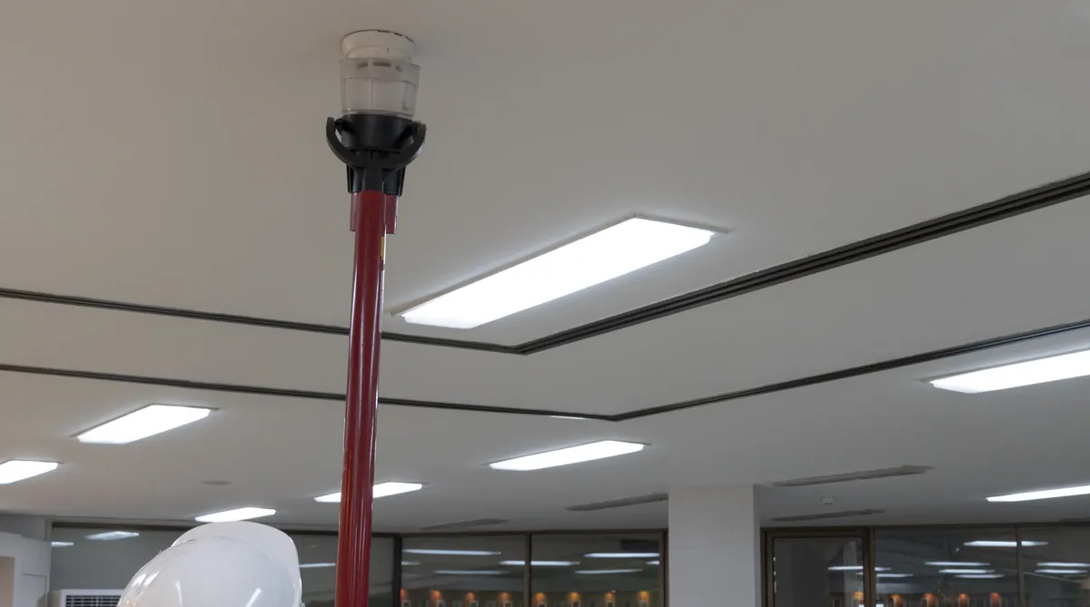 Technician testing a ceiling smoke detector with a tester pole in an office building